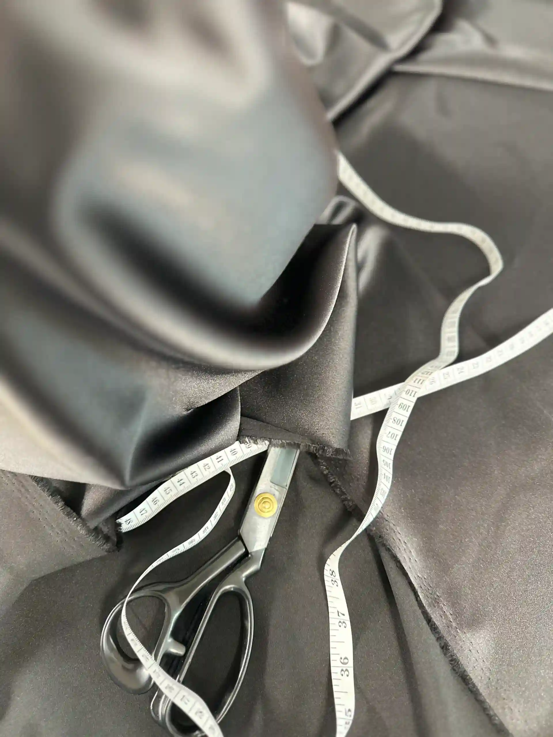 Bespoke tailoring from scratch: Scissors and a measuring tape on dark fabric.
