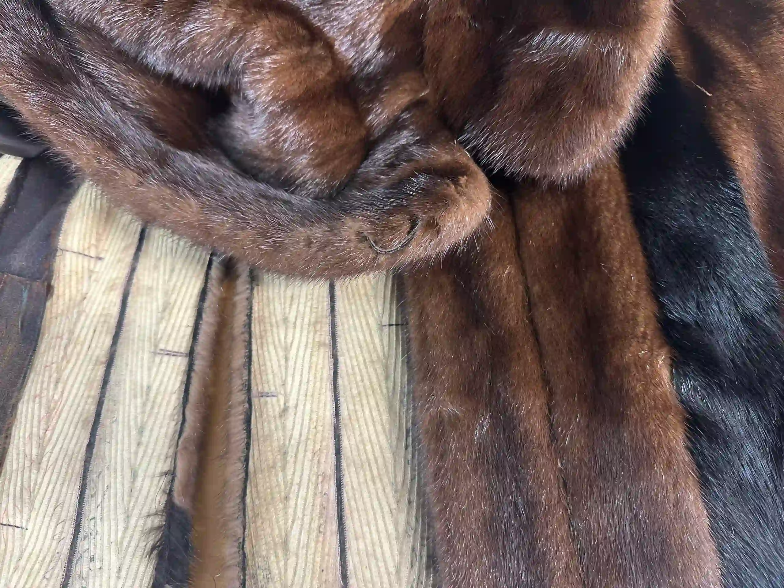 A detailed close-up of a luxurious dark brown and black fur coat undergoing alteration in the K&K Couture atelier. The image highlights the rich, plush texture of the fur pelts, intricate seaming, and the striped internal lining, showcasing the complex craftsmanship involved in expert fur tailoring.